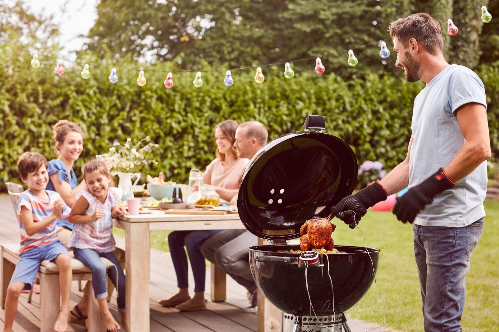 Rodzina z dziećmi, siedząca przy ogrodowym stole przy grillu.